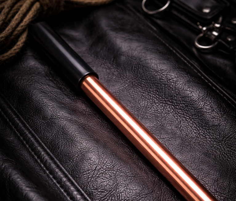 copper industrial impact cane resting on black leather with rope and hardware
