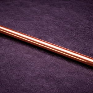 straight copper discipline cane with black handle resting on black leather surface