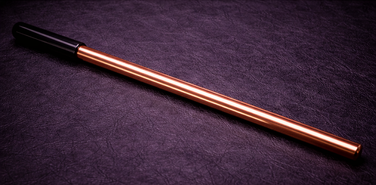 straight copper discipline cane with black handle resting on black leather surface