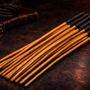 set of natural kooboo rattan discipline canes with black grips on dark leather surface