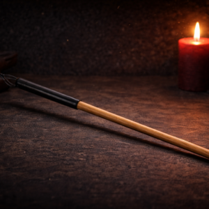 slender hardwood discipline cane with black grip resting on dark leather surface