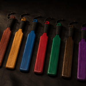 Collection of handcrafted Short Hardwood Paddles in multiple oak stain colors displayed on a black leather background.